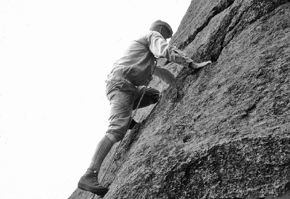 John Brett climbing an inclined rock face in the mountains.