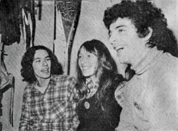 Black and white close-up of two young men and a young woman smiling for the camera.