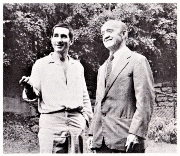 Vintage photo showing two men talking together; the man at left is pointing at something unseen in front of them.