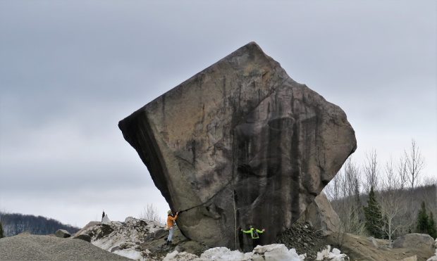 A huge square-shaped boulder about 12 metres high with two people inspecting it from below.