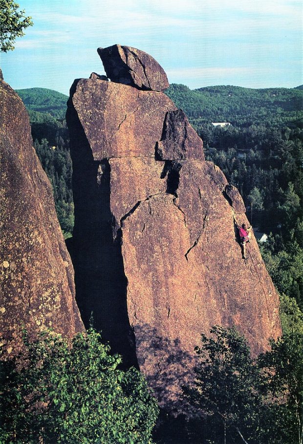 View of a young woman hanging on with hands and feet on the Mount Condor Needle, a huge brownish-orange rock formation some 23 metres in height.