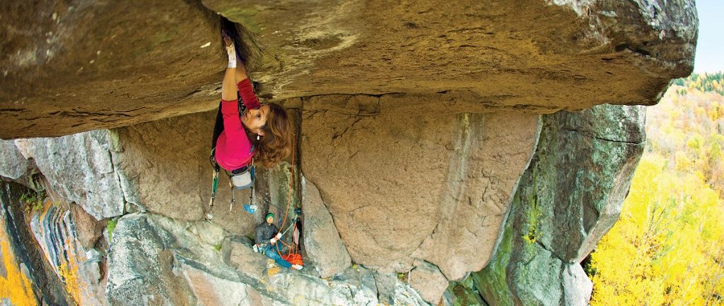 Close-up of a woman hanging on with hands and feet to the underside of an overhang with some 15 metres of reach