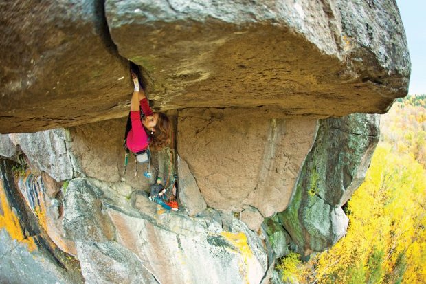 Close-up of a woman hanging on with hands and feet to the underside of an overhang with some 15 metres of reach