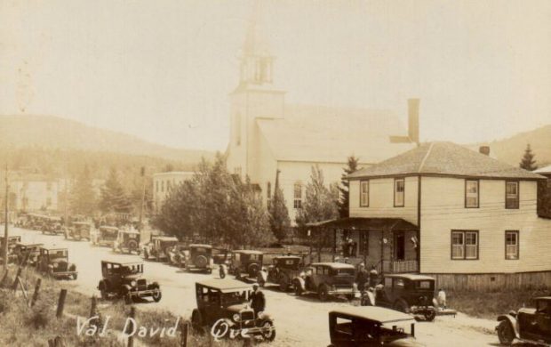 View of the village of Val-David in 1929 showing the main street. the church and old cars.