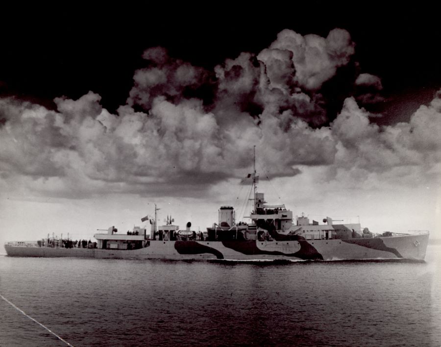 Black and white photograph of a ship on the water. Above, a dark cloud-filled sky.