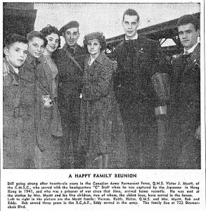 Black and white newspaper. Photograph at a train station, in the centre a soldier and his wife. On the left, two boys and a girl, on the right, two men in uniform. Below, a 125-word article titled “A Happy Family Reunion.”
