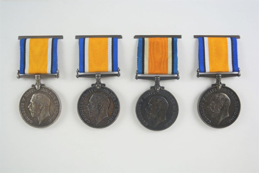Photographie de l’avers de quatre médailles de couleur argent avec l’effigie de Georges V de profil et une inscription, attachées à un court ruban composé de 7 bandes verticales (bleu, noir, blanc, orange, blanc, noir, bleu). 