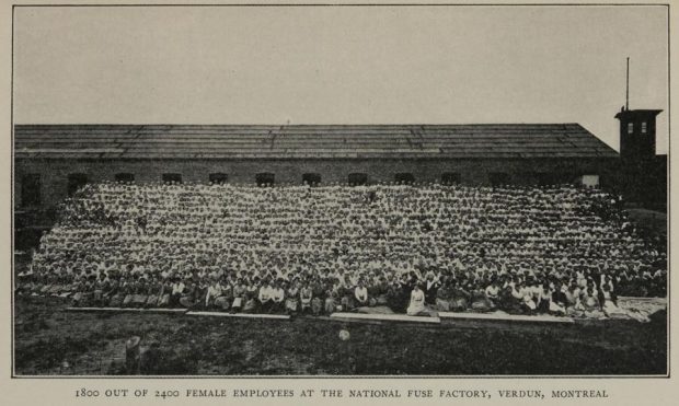 Black and white photograph of 1800 women sitting in some 20 rows on a small hill in front of the British Munitions Supply Company.