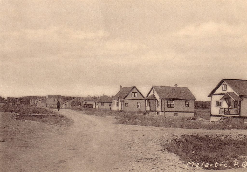 Photographie en sépia de plusieurs résidences alignées d’un seul côté d’une rue non pavée. Au centre, un homme marche.  En bas à droite, il est inscrit « Malartic. P.Q. ».