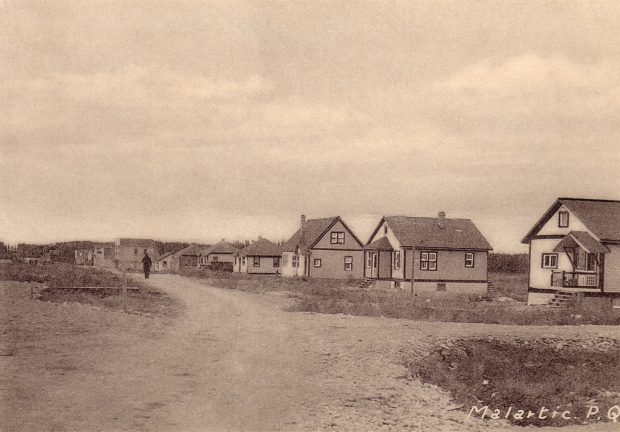 Sepia photograph of several residences lined up on one side of an unpaved street. In the centre, a man is walking. The inscription at the bottom right reads, Malartic. P. Q..