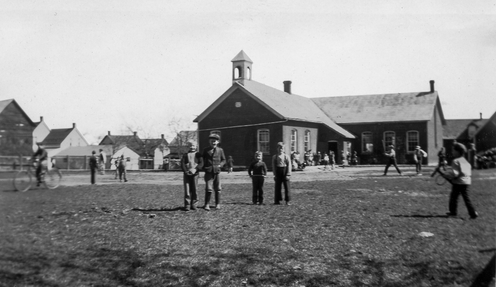 Children play in front of a brick school building equipped with a small bell tower.