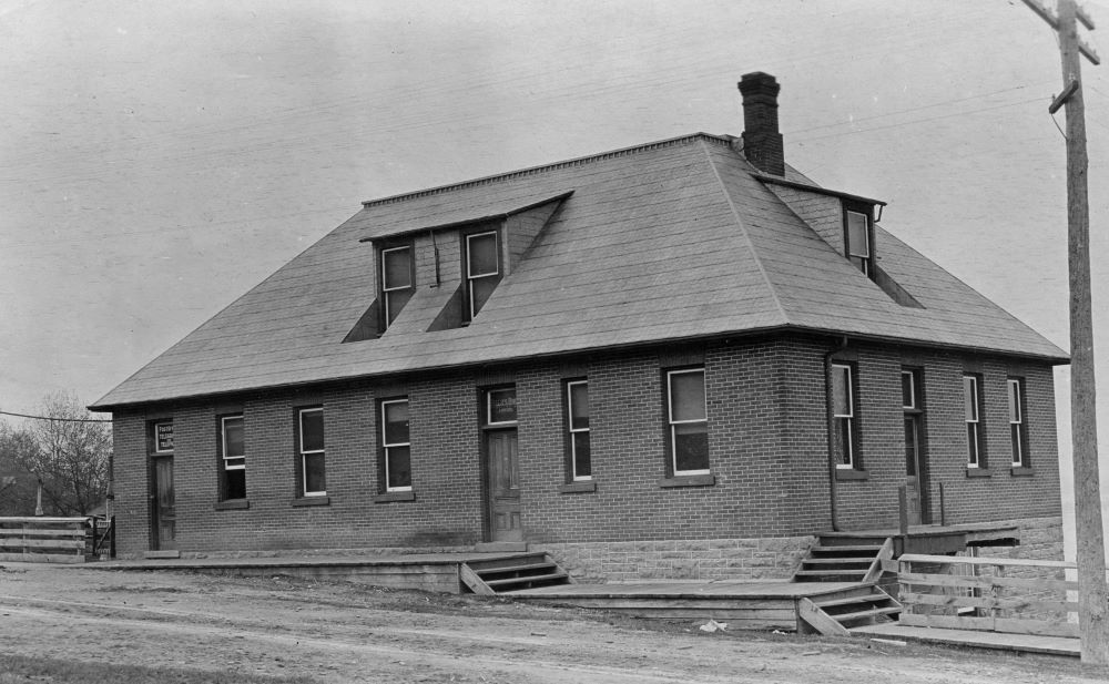 A brick office building with three wooden doors and multiple windows sits on the side of a hill.