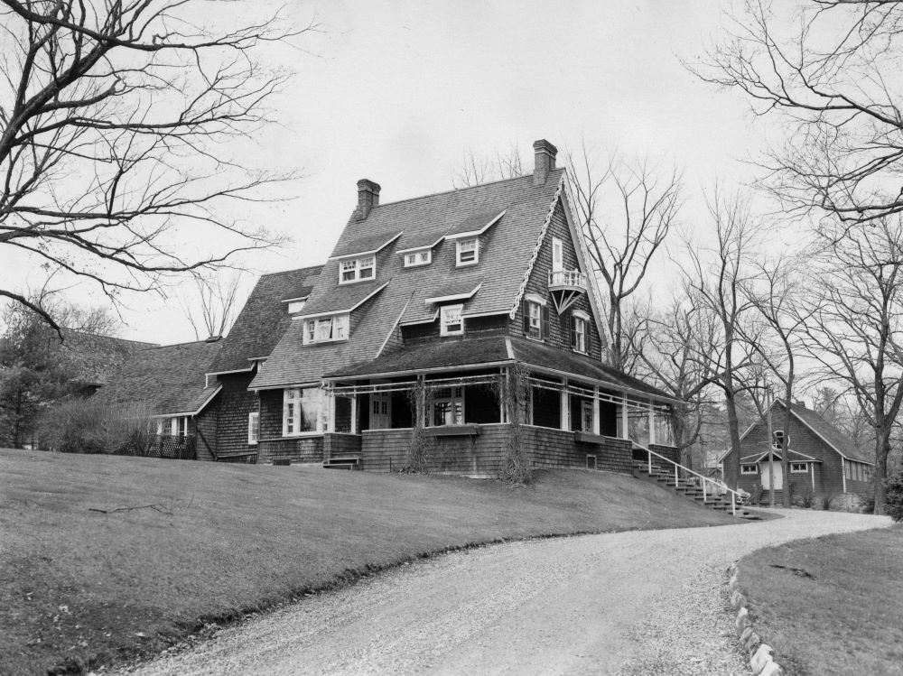 A winding road leads to a home with a steeply pitched roof covered in cedar shingles.