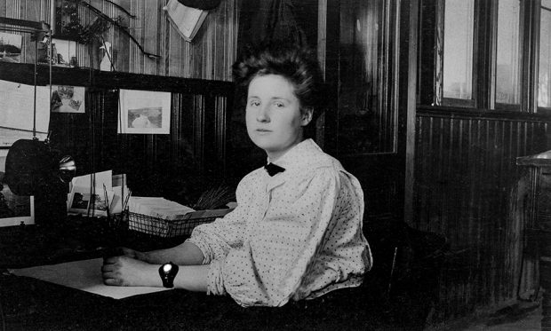 A young woman sits at her desk in an office lined with wooden panels.