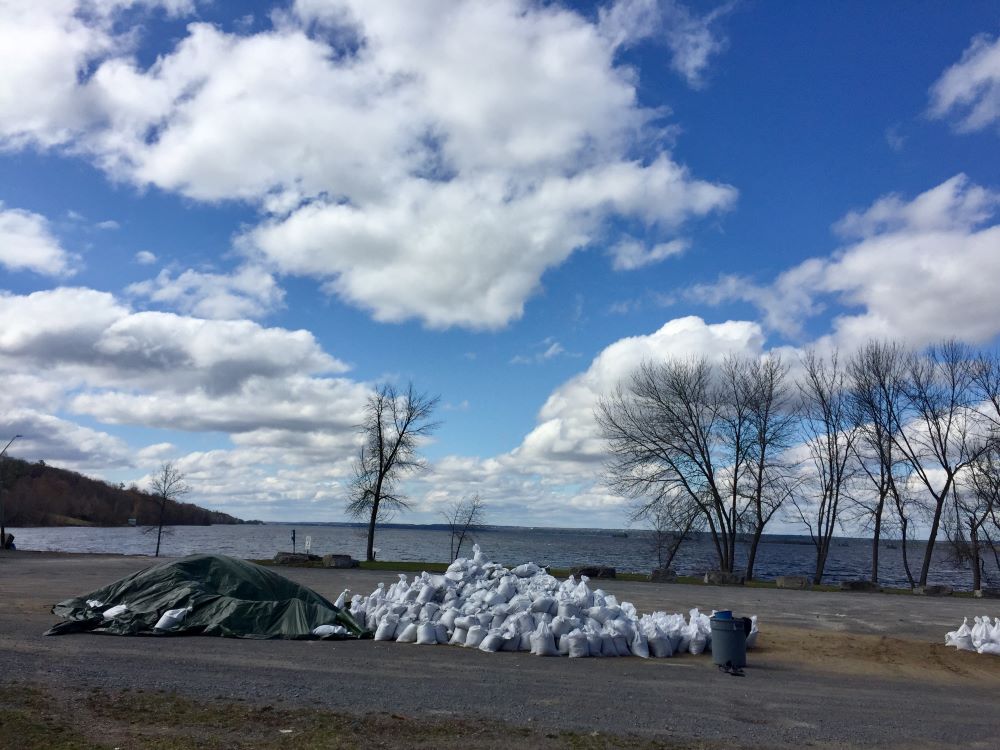 Two large piles of sand bags located in a parking lot near the river are ready for use.