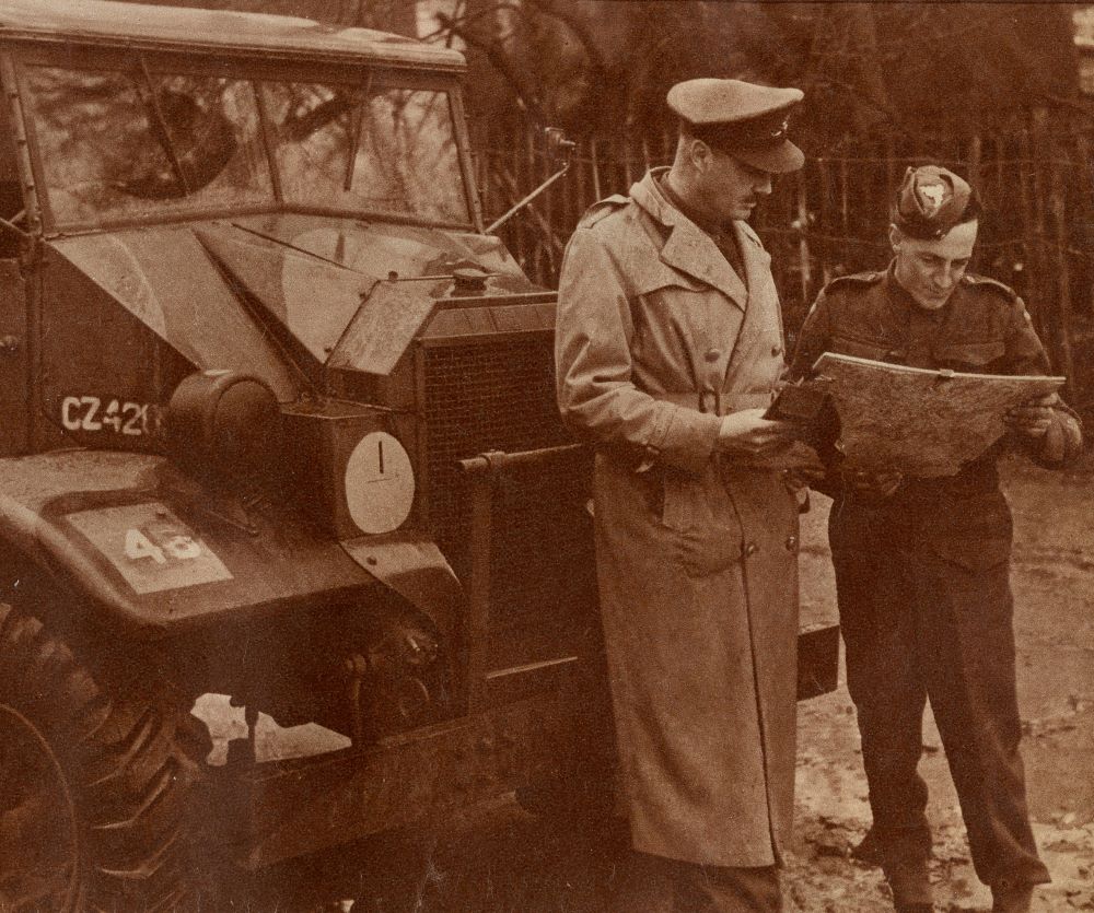Magazine clipping showing two men in WWII uniforms stand in front of an army tank looking at a map.