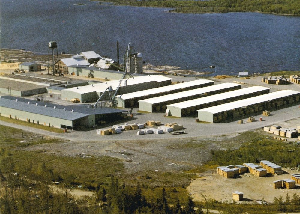 An aerial photograph shows Gillies Bros. mill site in summertime with log booms near shore.