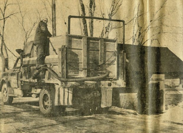 Newspaper clipping shows a man standing on the side of a truck while water is being pumped in from a pipe above.