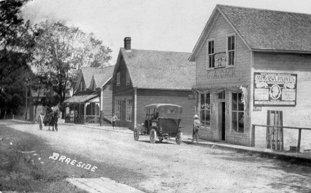 Post card of Braeside shows village street scene with people, stores, a horse drawn carriage an early automobile.