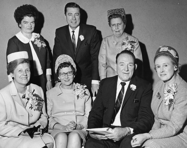 A black and white photo of five women and two men. The group is elegantly dressed, including corsages.