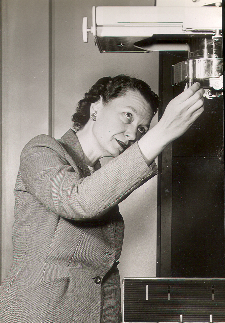 A black and white photo of a woman in a suit adjusting a piece of medical equipment.