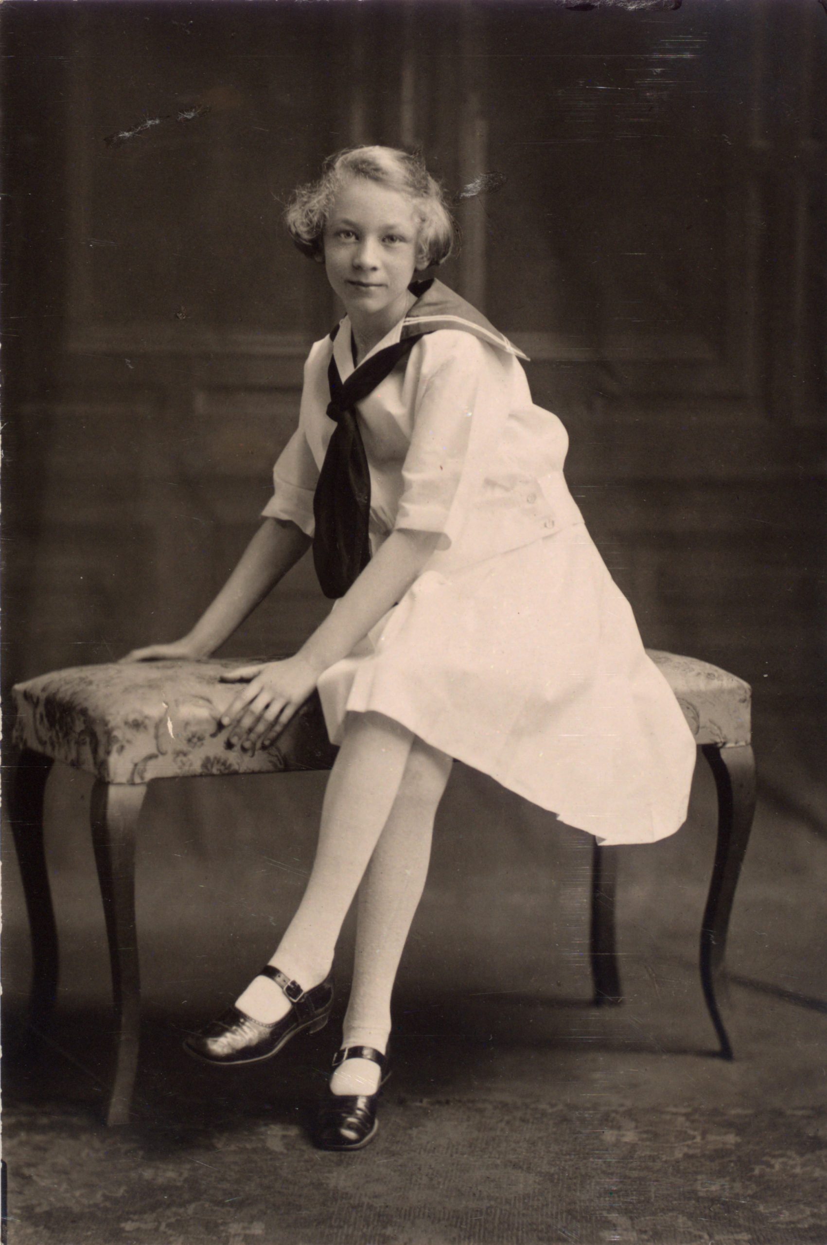 A black and white portrait of a young lady seated on a bench.
