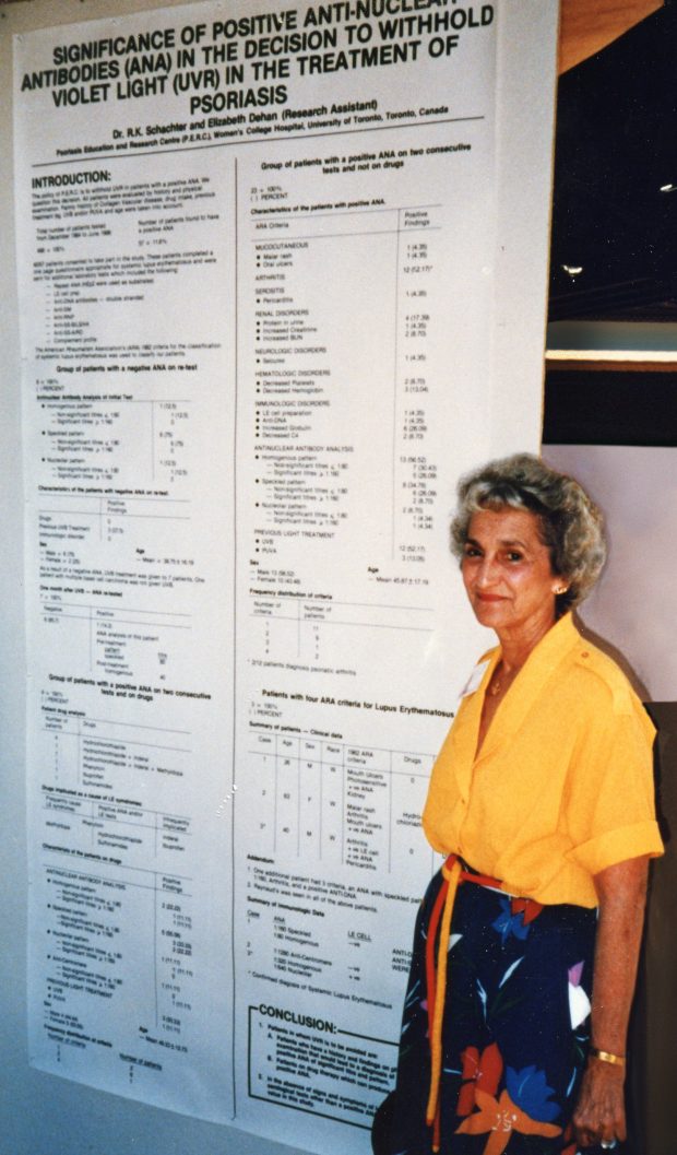 A coloured photo of a woman posing in front of a large poster board.
