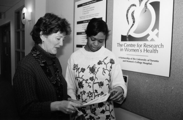 Two women examine a brochure; a large sign on the wall by them reads The Centre for Research in Women's Health.