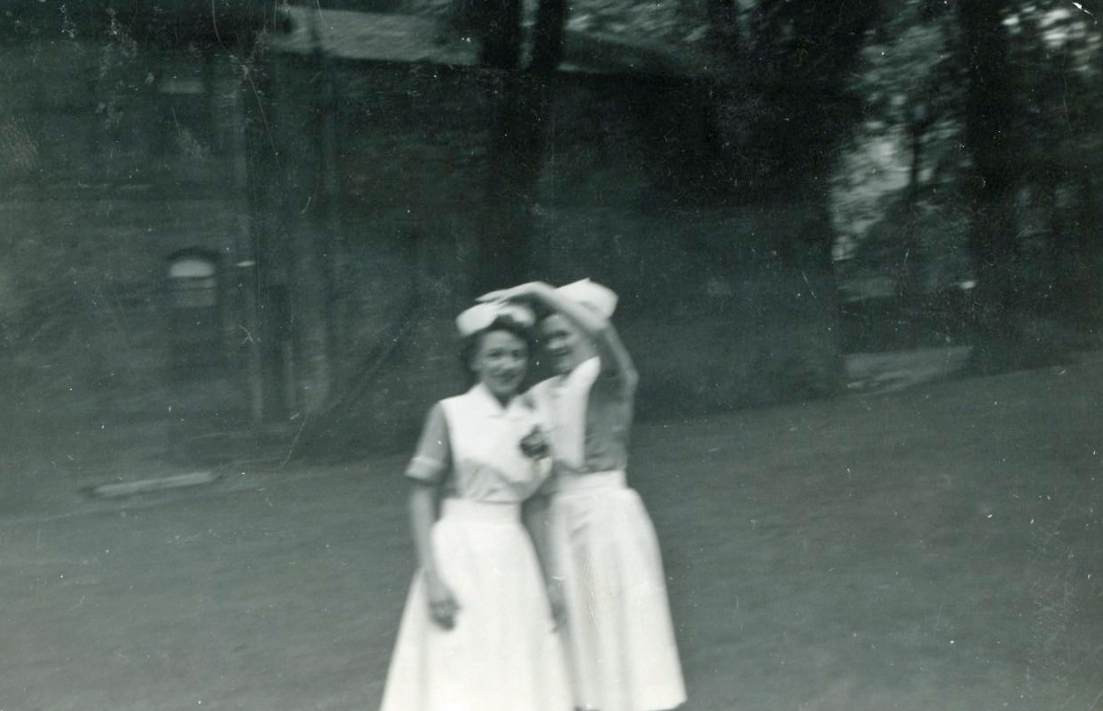 Two smiling women outside, in nurses' uniforms.