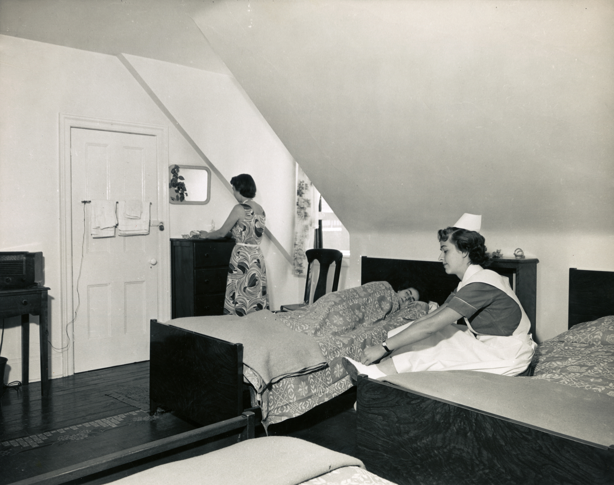 A woman in a dress before a mirror, another in nurse's uniform sitting on a bed, and a third sleeping. Three beds in the room.