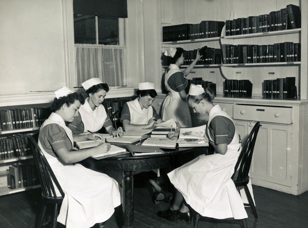 Four women at a table piled with books. A fifth reaches for a bookshelf.