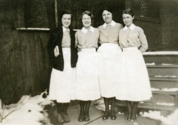 Four smiling women in long white skirts and light blouses.