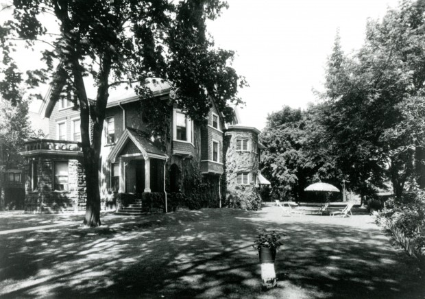 A vine covered home surrounded by trees, and including a generous lawn.