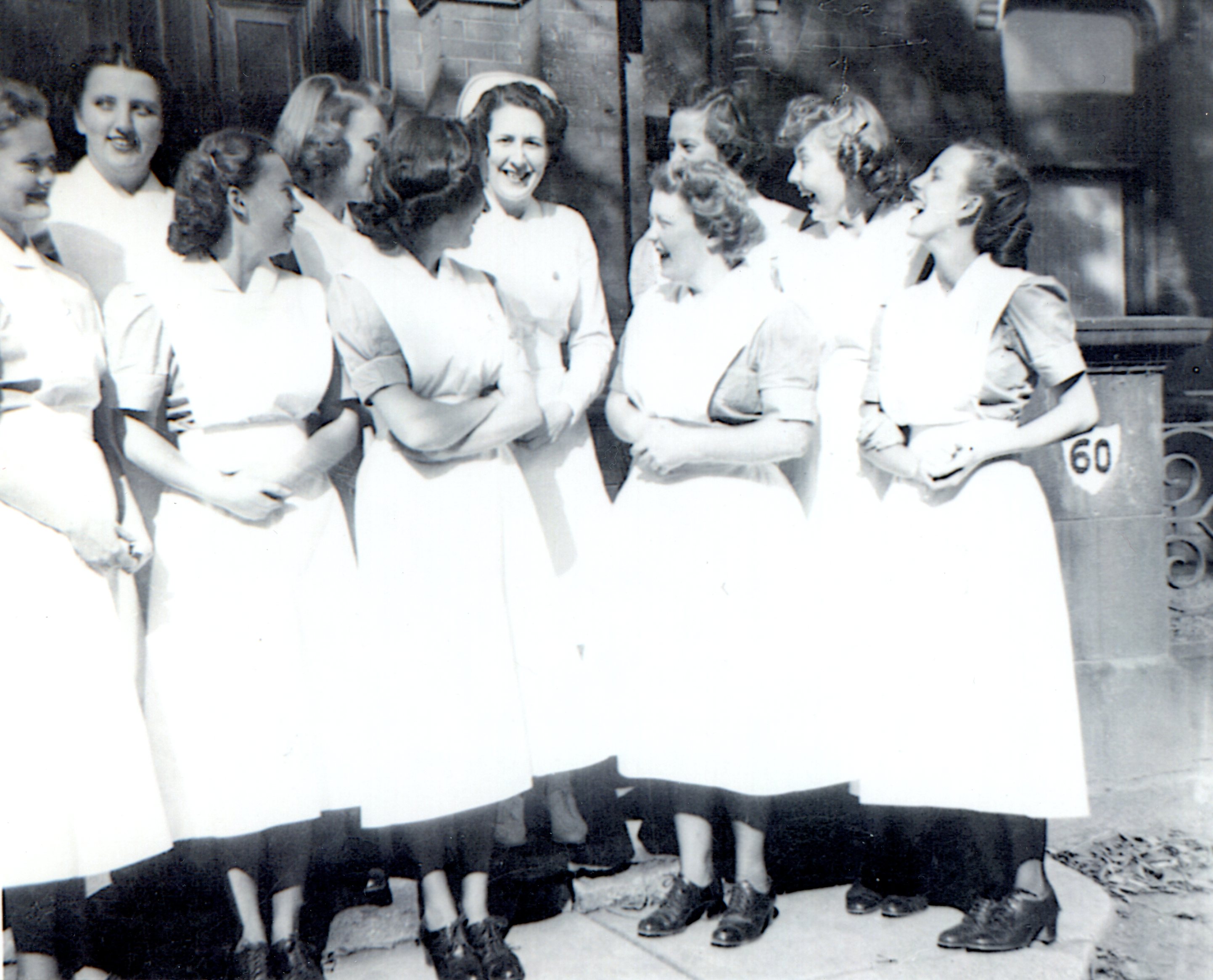 Ten laughing young women in uniforms. One is wearing a nurses' cap.