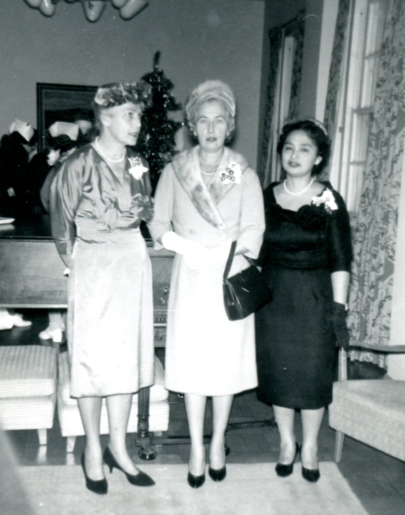 Three women pose for the camera. They are dressed up, and have corsages.