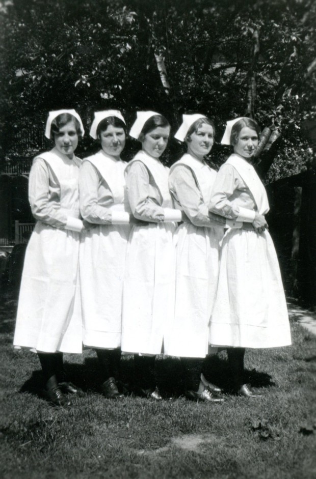 Five young women pose outside for a formal photograph. They are wearing nurses' uniforms and caps.