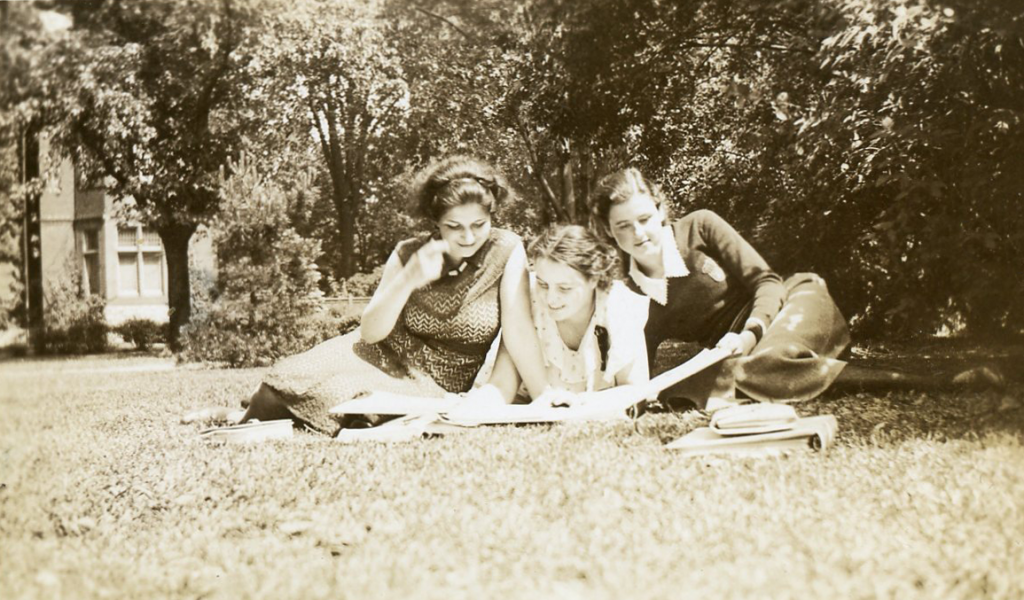 Three young women dressed casually are studying in a park.