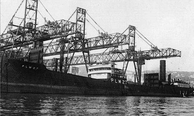 a large steel cargo ship moored at a loading wharf with large cranes