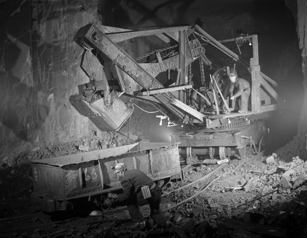 Power shovel loading iron ore into an ore car and two workers in a mine shaft