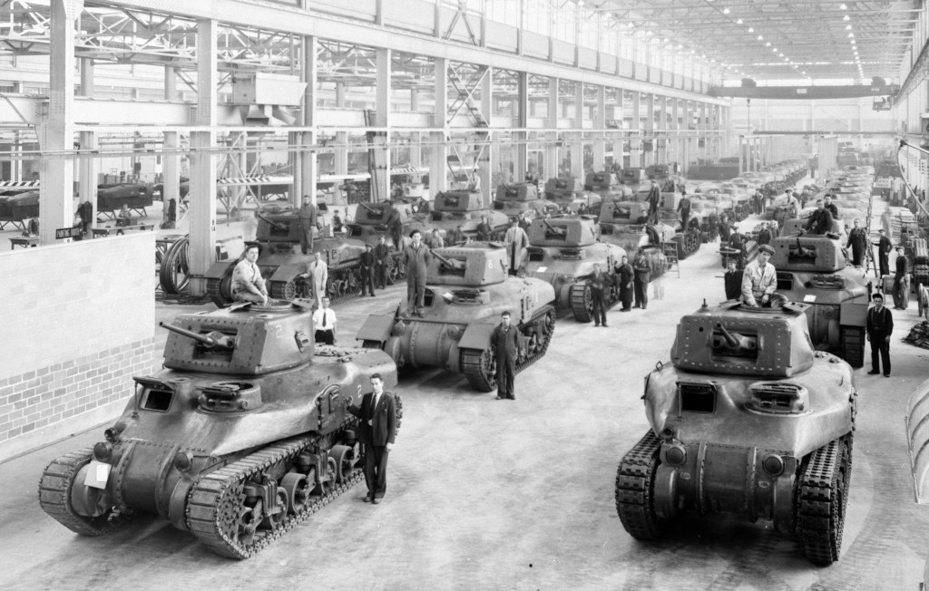 three rows of dozens of army tanks and workers in a factory