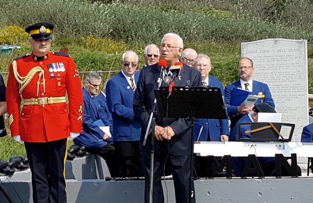 a man in blue suit talks into microphone at a remembrance ceremony with an RCMP police officer beside him
