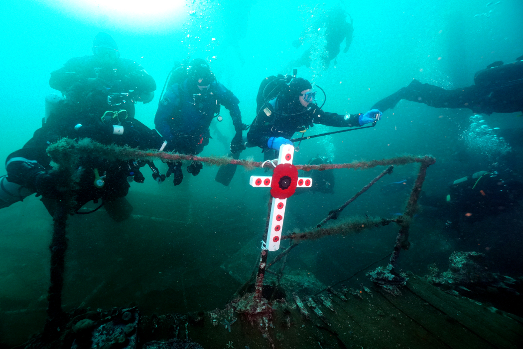 Group of scuba divers on underwater shipwreck near a cross with poppies