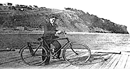 teenage boy in suit stands with his bicycle on a wharf