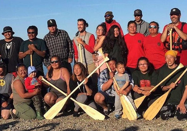 Group of smiling men and women holding canoe paddles.