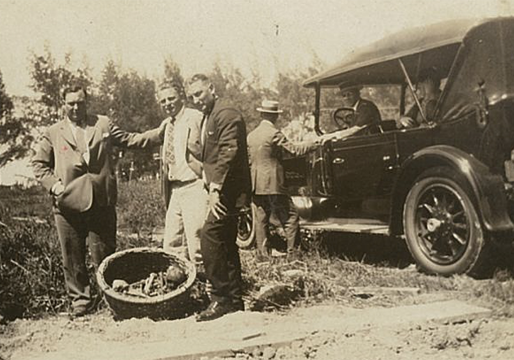 Three men pose in front of a vintage car.