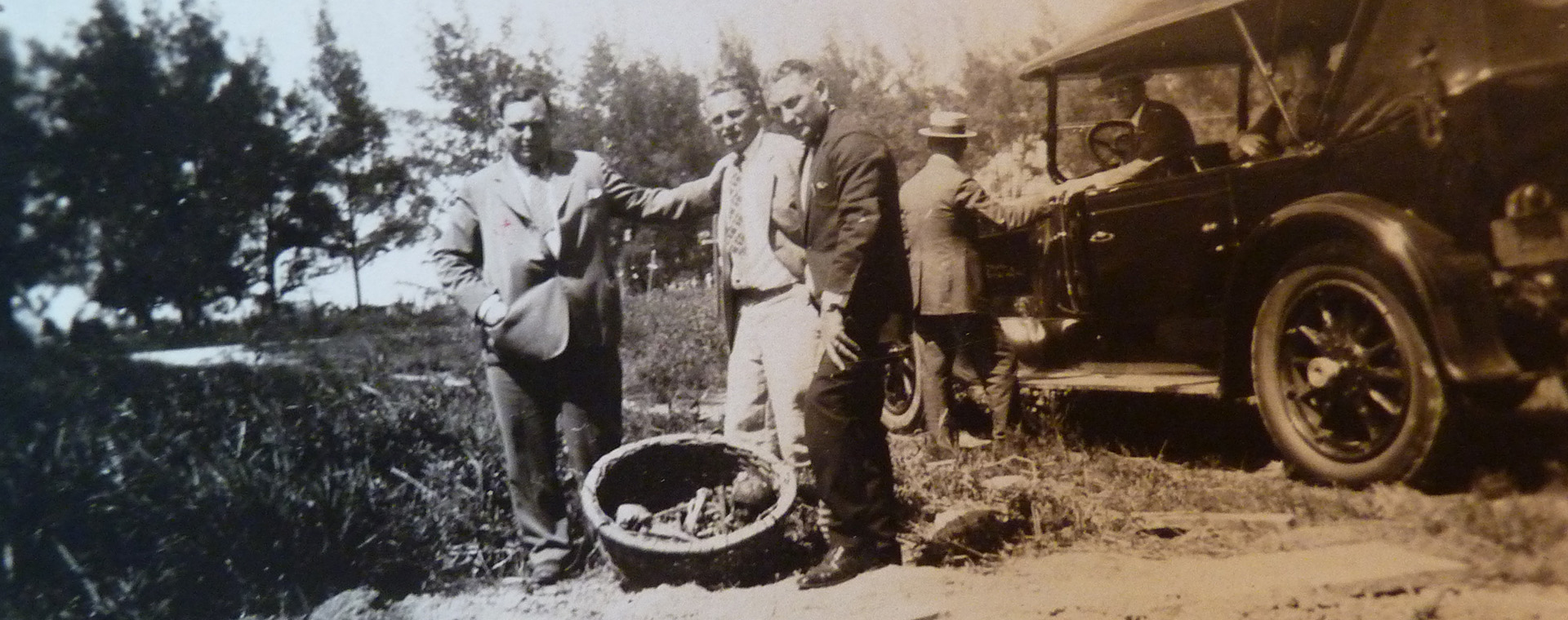 Three men pose in front of a vintage car.