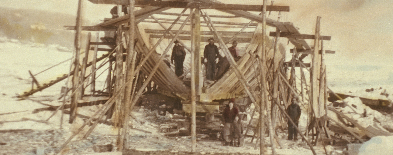 View of a schooner under construction. The structure of the ship is surrounded by scaffolding.