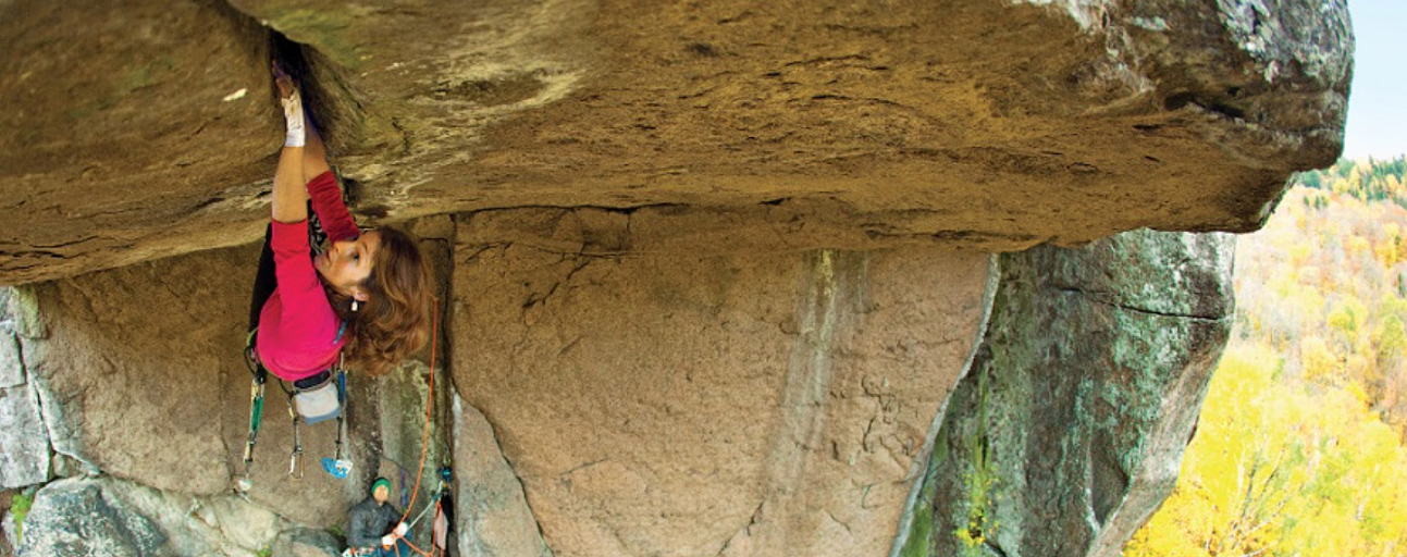 Close-up of a woman hanging on with hands and feet to the underside of an overhang with some 15 metres of reach