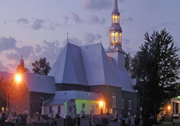 Color photograph, long shot taken at night, back view of church, presbytery and cemetery, the exterior lights of the church are lit.