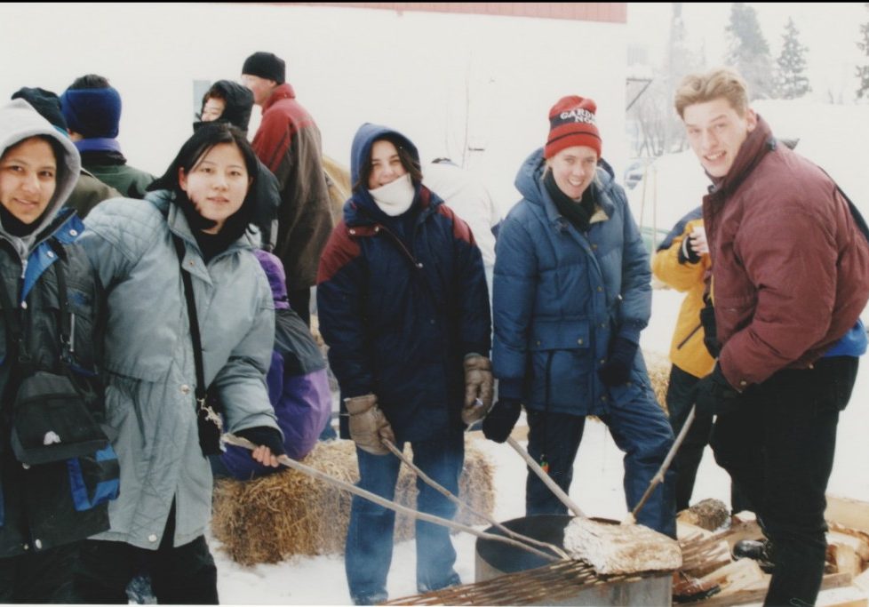 A number of young people dressed in winter gear roasting bannock over a fire. The activity was part of the 1999 Trappers' Festival.